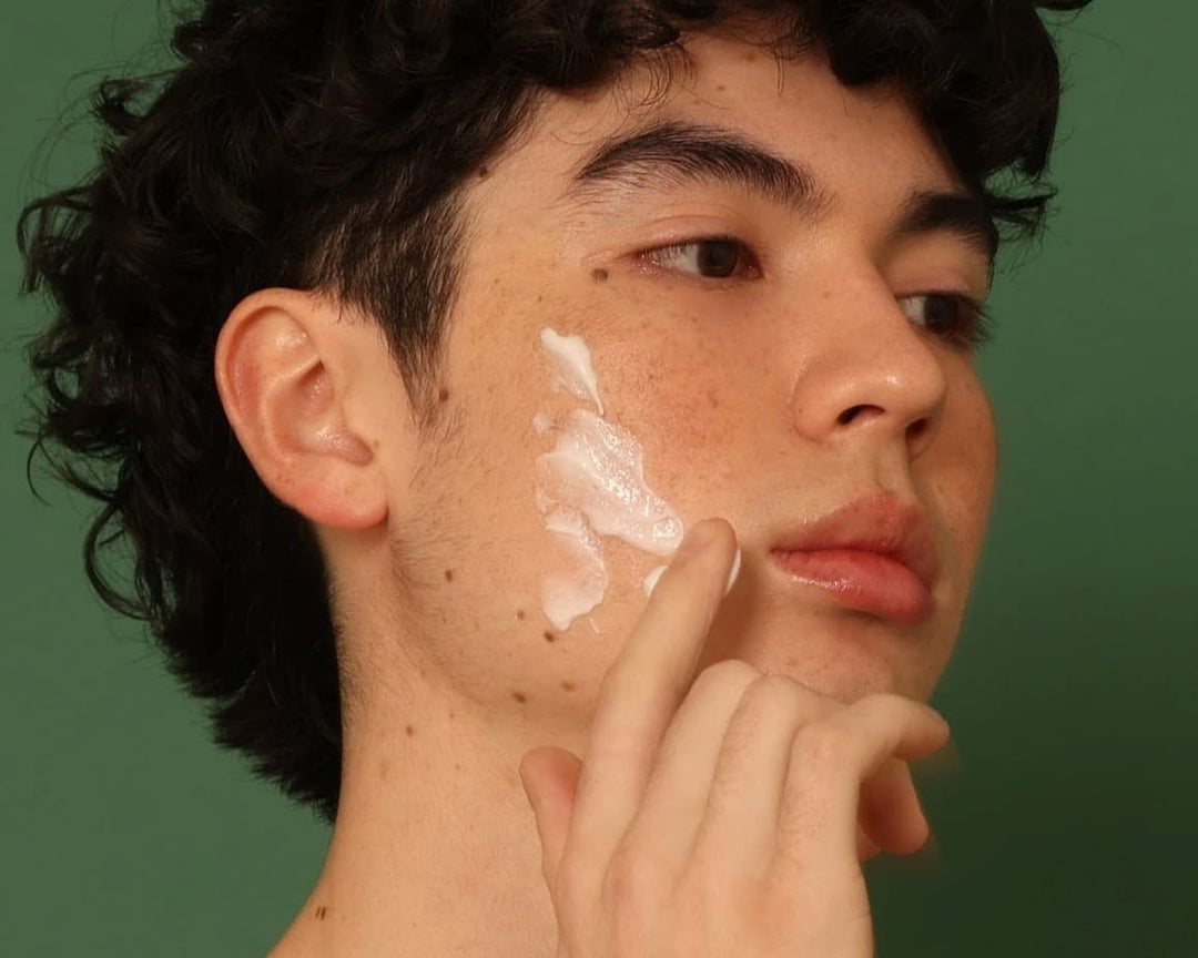 Man applying Stay Clear Beauty Sun Shield Sheer Sunscreen SPF 30 to his face on a green background — lightweight mineral sunscreen for acne-prone skin, sensitive skin, and daily broad-spectrum UV protection.