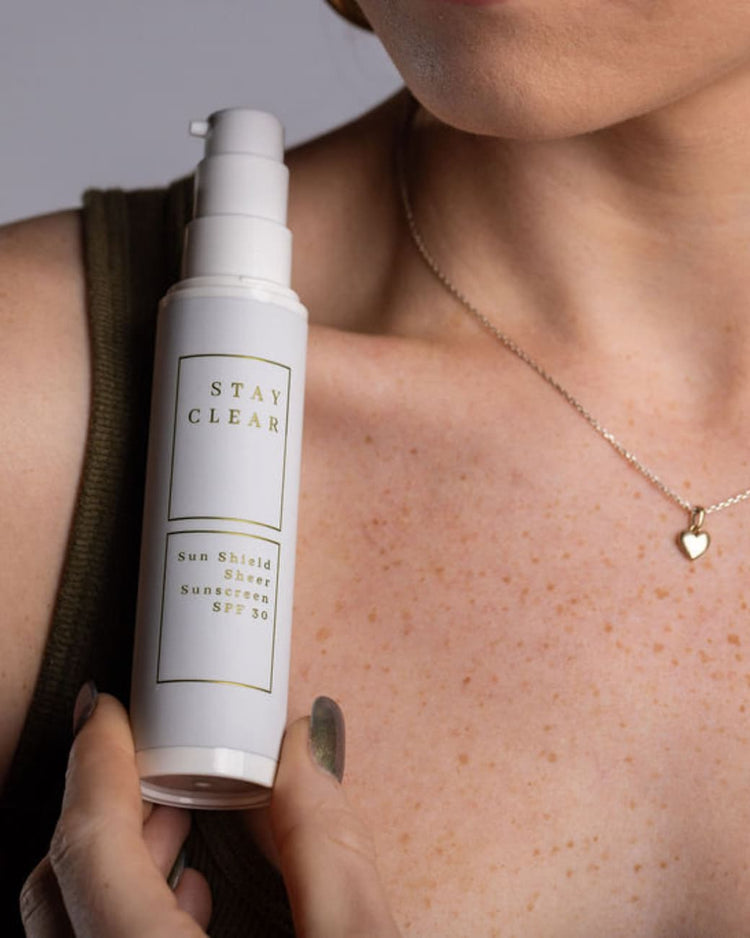 Stay Clear Beauty Sun Shield Sheer Sunscreen SPF 30 held by a model with clear, lightly freckled skin — mineral sunscreen for acne-prone skin, sensitive skin, and daily UV protection.