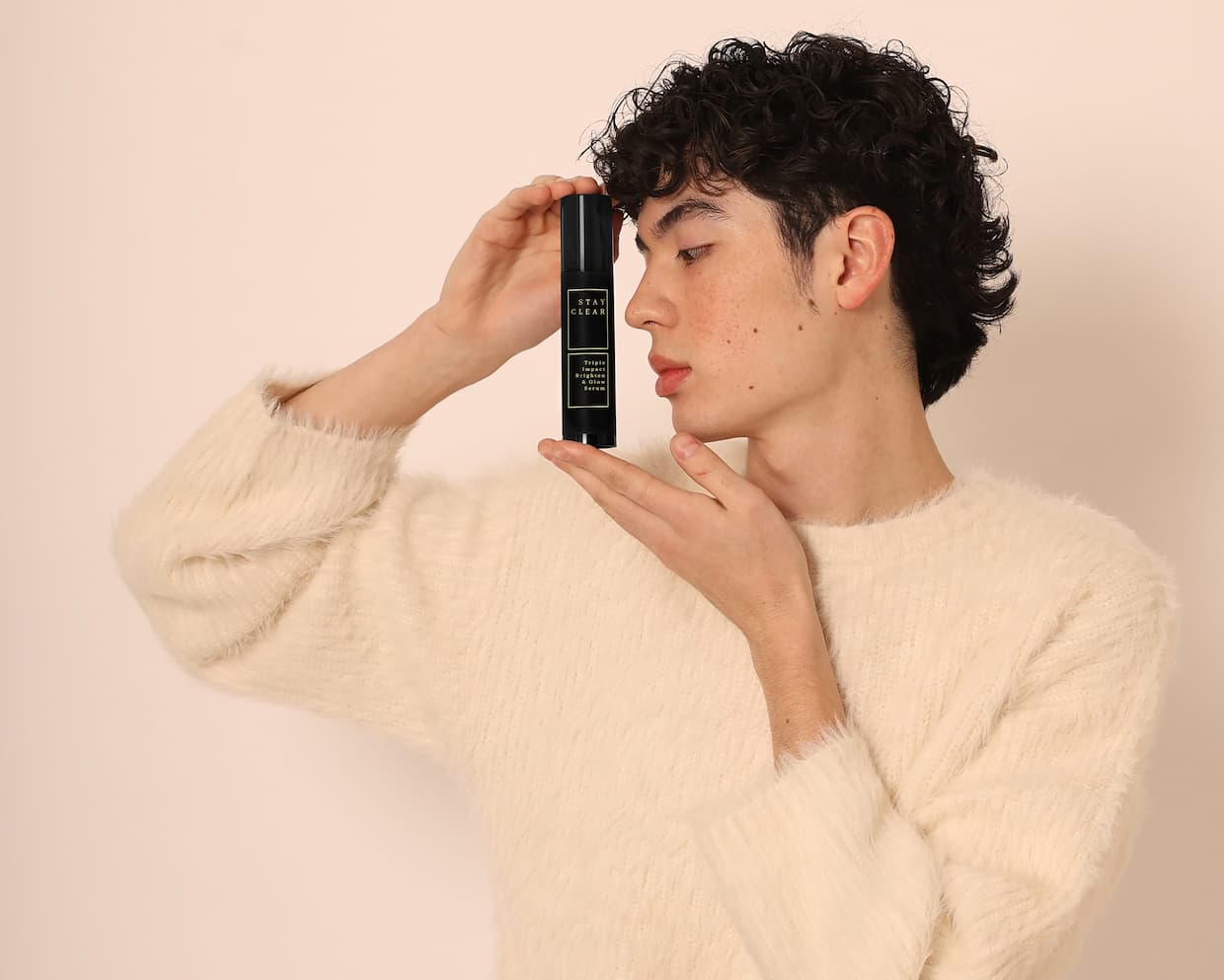 Young man with clear skin holding Stay Clear Beauty Triple Impact Brighten & Glow Serum airless pump bottle — brightening serum for dark spots, post-acne marks, hyperpigmentation, and uneven skin tone.