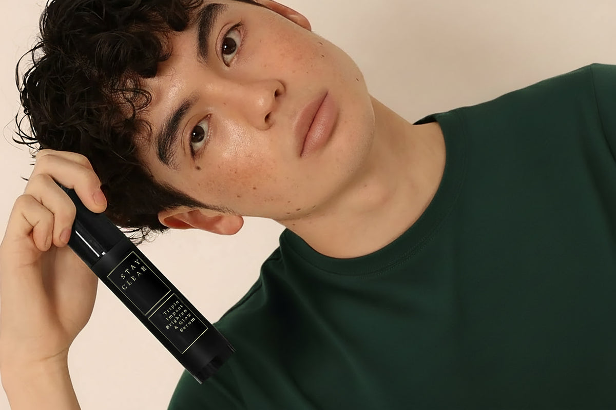 Man in a green shirt holding Stay Clear Beauty Triple Impact Brighten & Glow Serum beside his face.