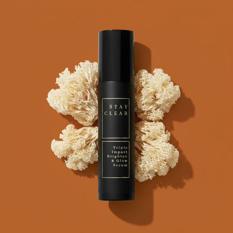Stay Clear Beauty Triple Impact Brighten & Glow Serum matte black airless pump bottle flat lay with snow mushrooms on burnt orange background — brightening serum for dark spots, age spots, post-acne marks, hyperpigmentation, and uneven skin tone.