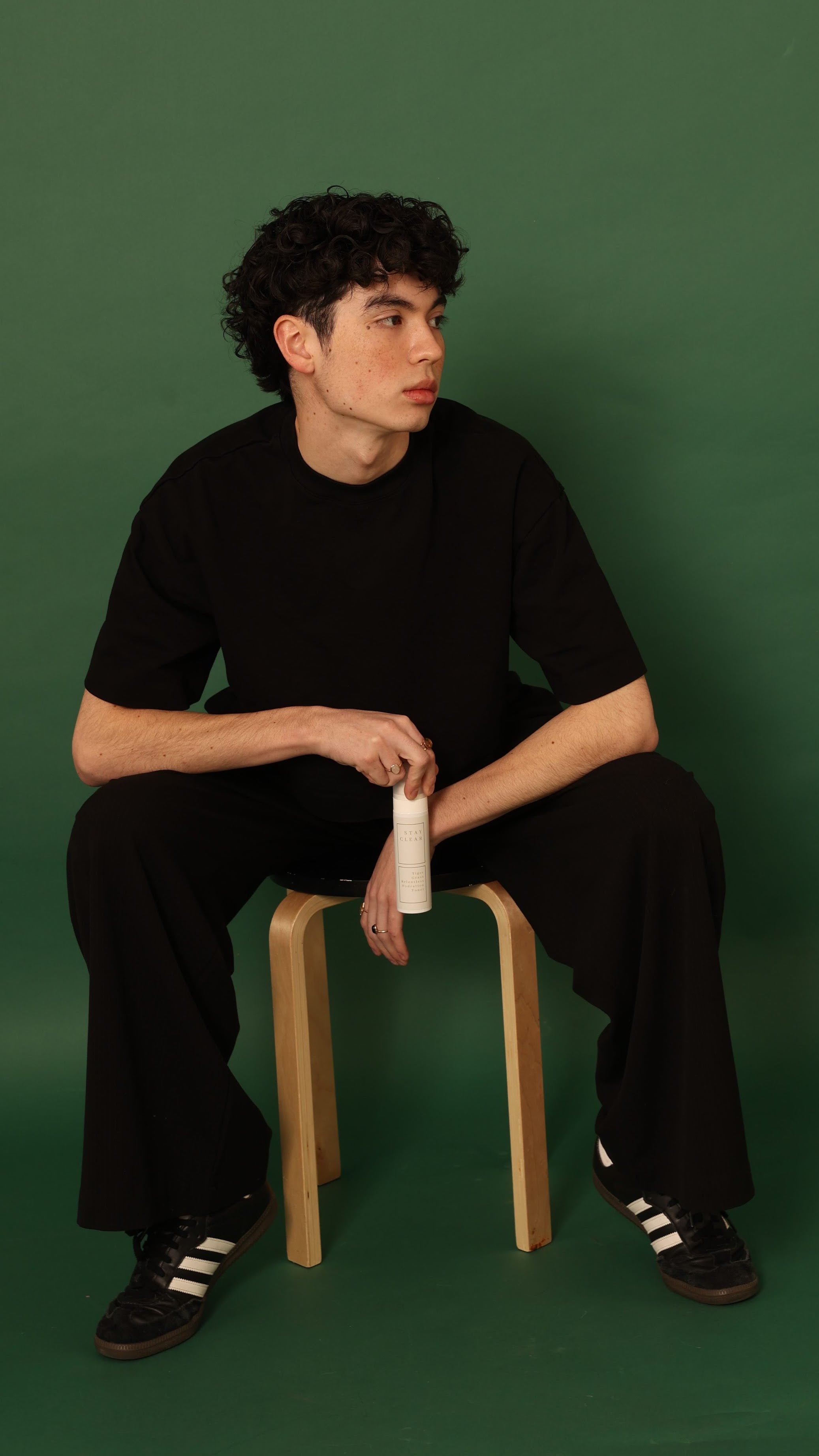 A man seated comfortably, holding Stay Clear Tiger Grass Relentless Hydration Toner, highlighting its soothing and moisturizing benefits for sensitive skin.