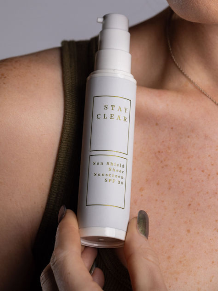 A woman holding Stay Clear Sun Shield Sheer Sunscreen SPF 30, highlighting its lightweight, broad-spectrum protection designed to shield the skin from harmful UVA and UVB rays while maintaining a sheer, natural finish.